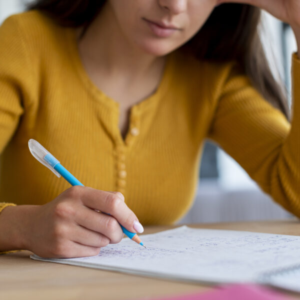 Mulher jovem estudando, segurando uma caneta azul e fazendo anotações em caderno, representando preparação para concurso público.