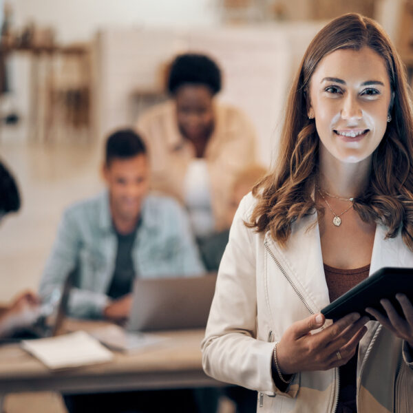 Mulher sorridente com tablet nas mãos em ambiente de trabalho colaborativo, representando uma profissional administrativa pronta para atuar no serviço público.